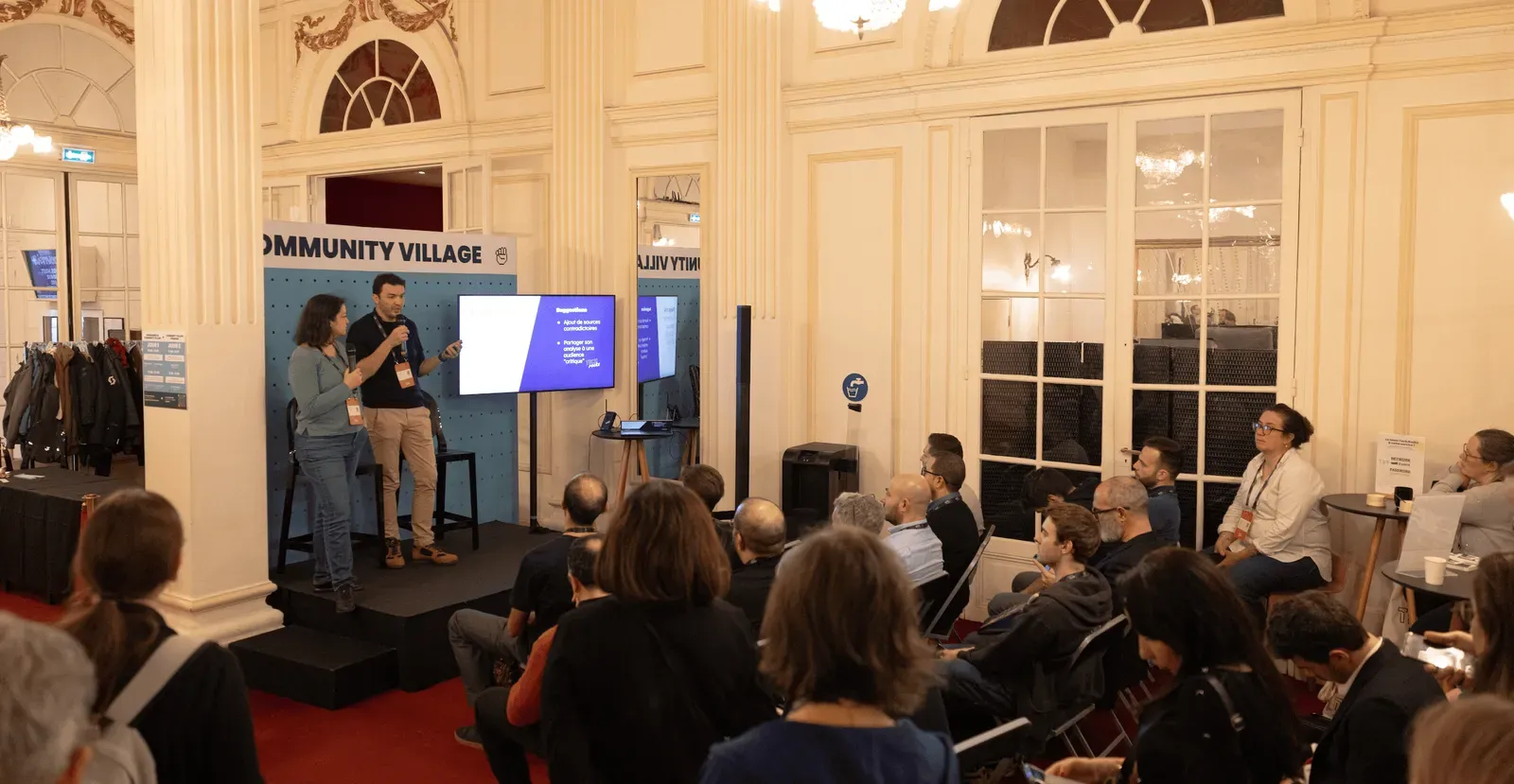 Session au Community Village du Tech.Rocks Summit : deux intervenant·es sur scène devant un écran, face au public assis dans un salon à moulures
