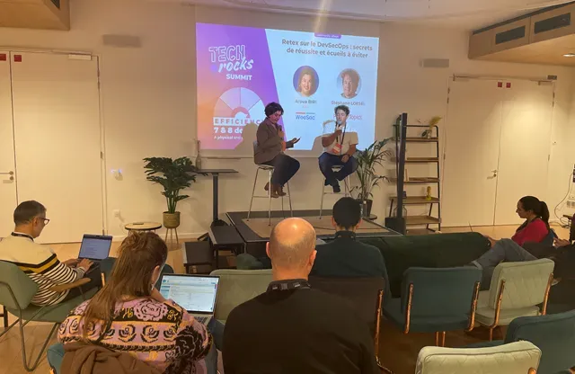 Interview sur scène au Tech.Rocks Summit, devant l’écran « Retex sur le DevSecOps : secrets de réussite et écueils à éviter », public installé avec ses ordinateurs