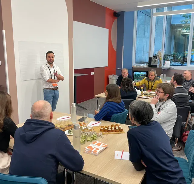 Atelier autour d’une grande table : un intervenant debout s’adresse à une dizaine de participant·es